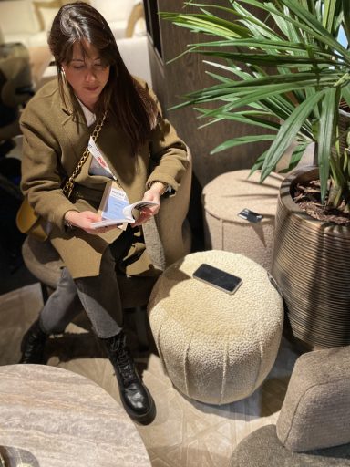 Femme assise sur un pouf, feuilletant un document, avec une plante en arrière-plan.