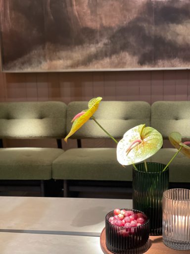 Fleurs dans un vase, gâteau chocolaté et coin de salle avec fauteuils verts.